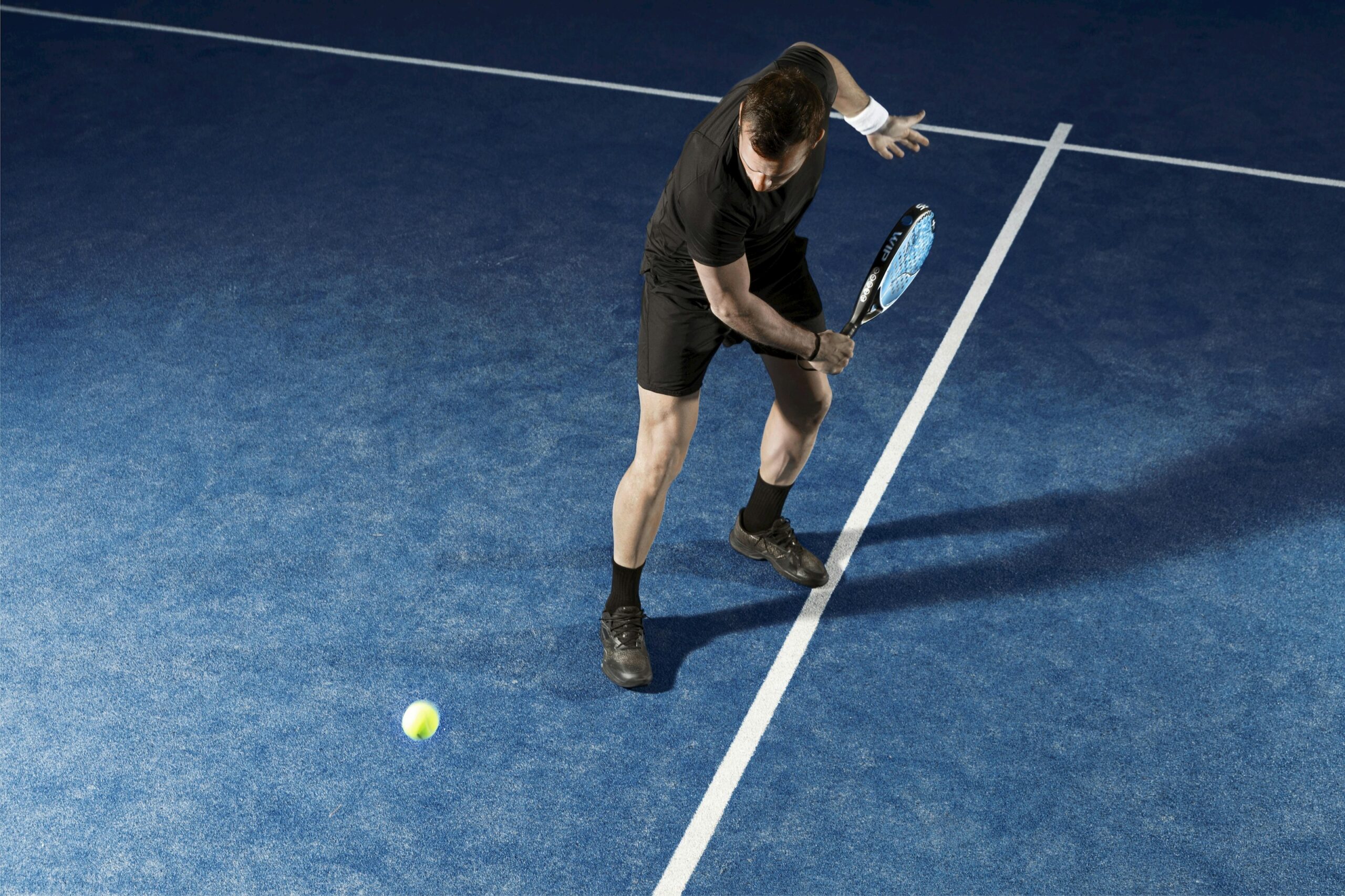 Player on an outdoor blue padel court — padel camps in Spain