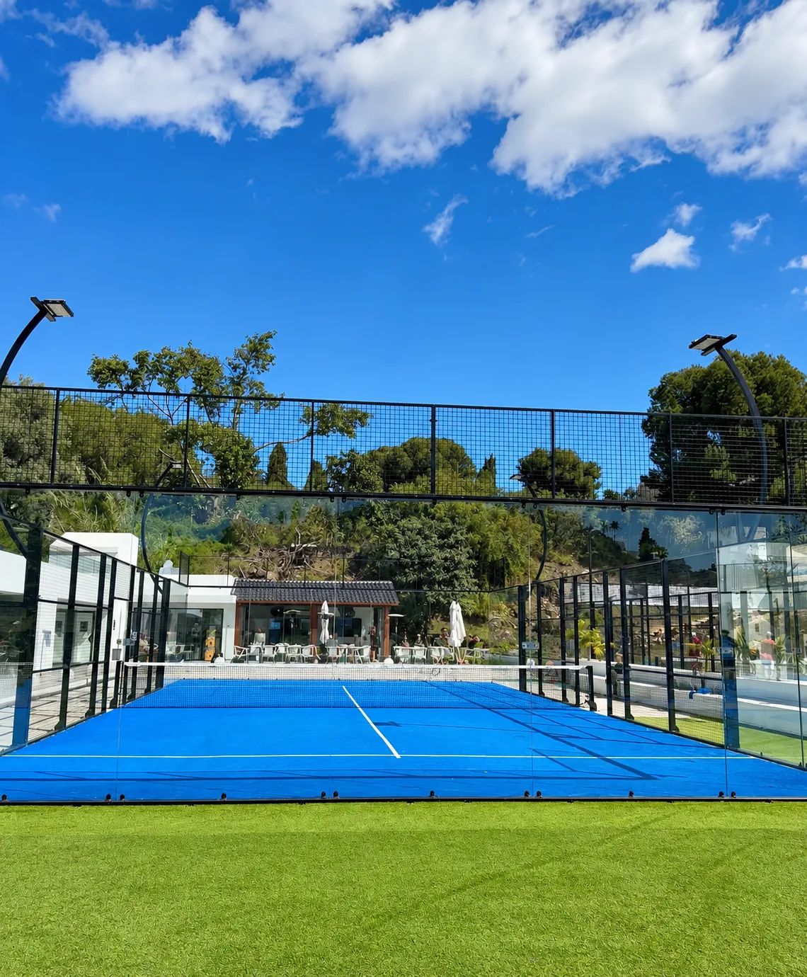 Blue padel court with glass walls under a sunny sky